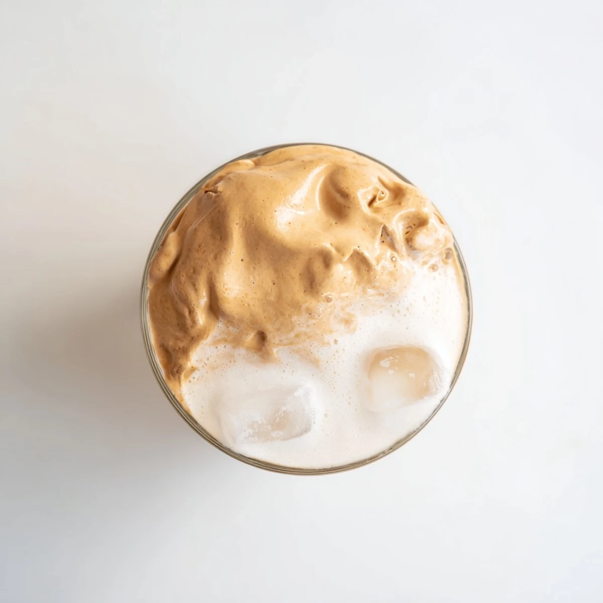 Two glasses of Dalgona coffee feature cloud-like whipped coffee floating over iced milk in a cafe-style presentation.  