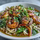 A close-up of an Asian Noodle Bowl with Shrimp and Scallops, featuring tender pink shrimp and golden scallops nestled among silky noodles, crisp snow peas, and vibrant bell peppers, all steaming in a savory broth.  
