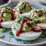 Vibrant deviled eggs filled with avocado and lime, topped with a zesty Sriracha kick for extra flavor.  