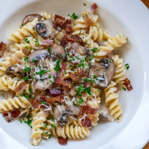 Golden fusilli with bacon, onions, and mushrooms, a comforting Italian-inspired pasta dish.