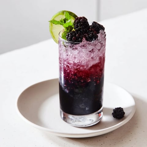 A refreshing Dark Matter Mocktail showing layered black drink, garnished with blackberries, and citrus.