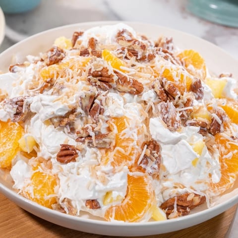 A vibrant bowl of Elevated Ambrosia Salad, showcasing mandarin oranges and toasted pecans in luscious whipped cream.