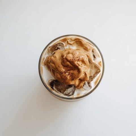 Fluffy whipped Dalgona coffee perched atop a glass of creamy milk, creating a striking layered beverage.  