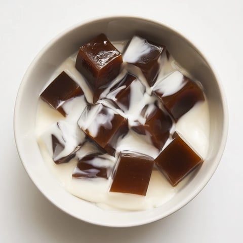 Cubes of dark coffee jelly glistening with light, layered in a glass and topped with a cloud of sweetened cream for a refreshing dessert.  