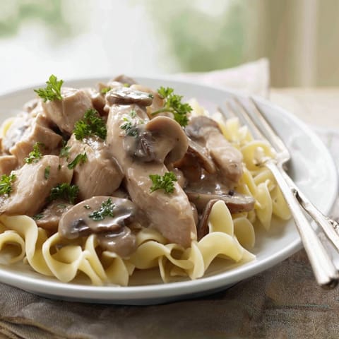 Tender strips of golden chicken and sautéed mushrooms swim in a creamy paprika sauce over egg noodles, offering comforting warmth.