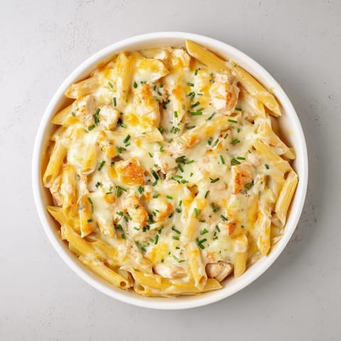 A serving of creamy Chicken Ranch Pasta Bake on a white plate, featuring tender penne pasta, shredded chicken, and a fresh chive garnish.  