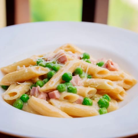 Steaming Spring Pea & Ham Pasta with golden-brown ham pieces and bright green peas in a glossy cream sauce.