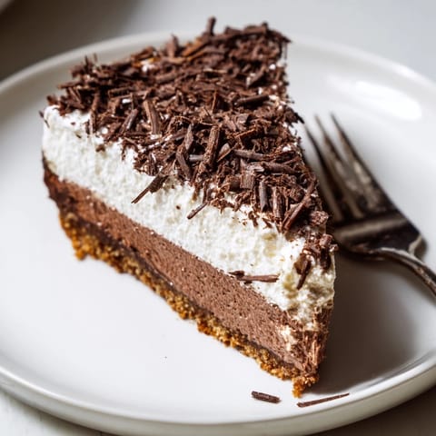 A slice of lighter chocolate cottage cheese cheesecake on a white plate with dark chocolate shavings and fresh berries.