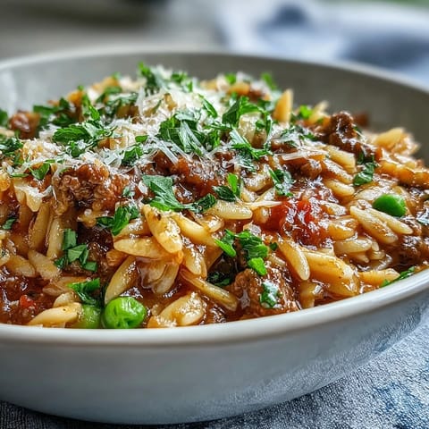 Bubbling Comforting Ground Beef Orzo Dinner in a skillet garnished with fresh parsley and melted Parmesan.