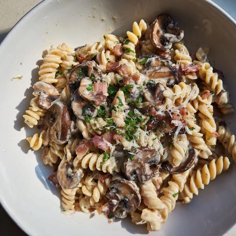 Perfectly cooked fusilli with bacon and mushrooms, topped with fresh parsley, ready to eat.