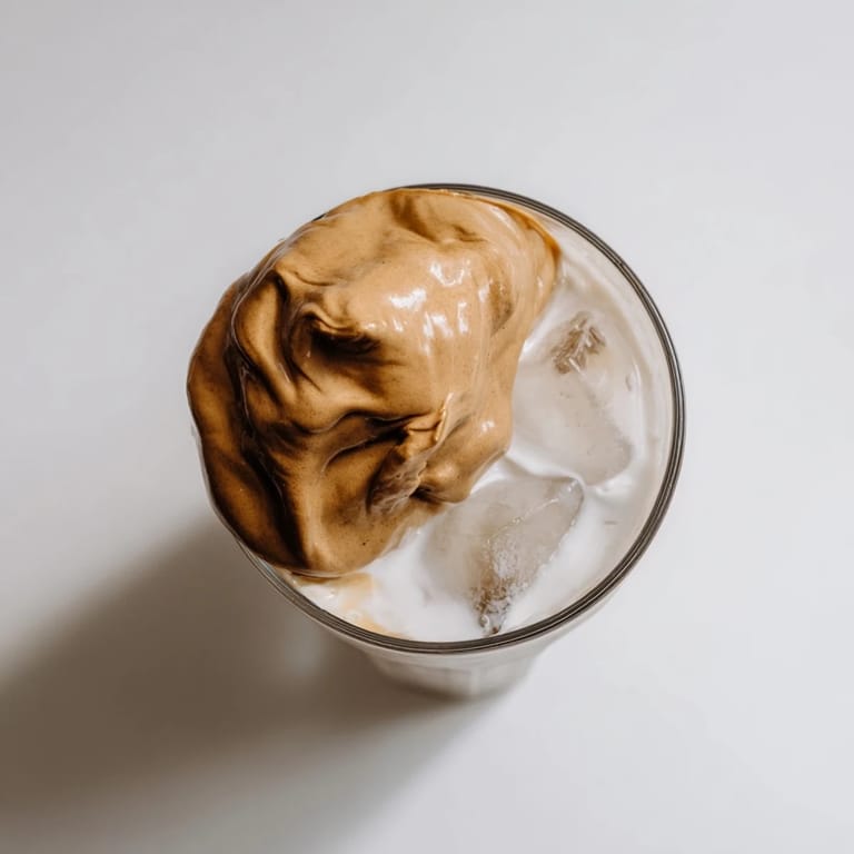 A creamy glass of Dalgona coffee with frothy whipped instant coffee topping, served over cold milk and ice.