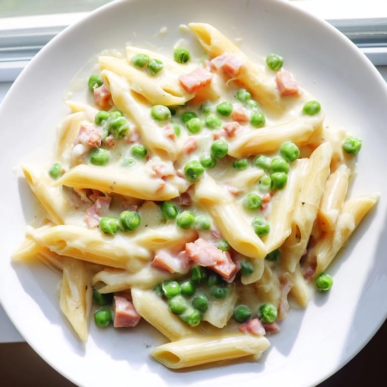 Freshly grated Parmesan sprinkled over a vibrant Spring Pea & Ham Pasta, garnished with chopped parsley on a rustic table.