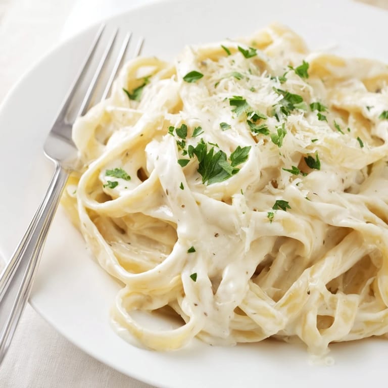 Steaming hot Easy Creamy Cauliflower Alfredo pasta twirls on a fork with velvety sauce and sautéed garlic.  
