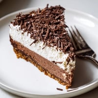 A slice of lighter chocolate cottage cheese cheesecake on a white plate with dark chocolate shavings and fresh berries.