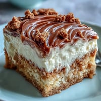 Decadent Baked Biscoff Cake with Creamy Lotus Frosting is shown on a white plate with a slice cut to reveal crumbled cookie chunks.