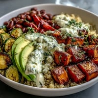 A vibrant Black-Eyed Pea Buddha Bowl with roasted sweet potatoes and red bell peppers on a bed of fluffy quinoa, topped with creamy avocado slices.